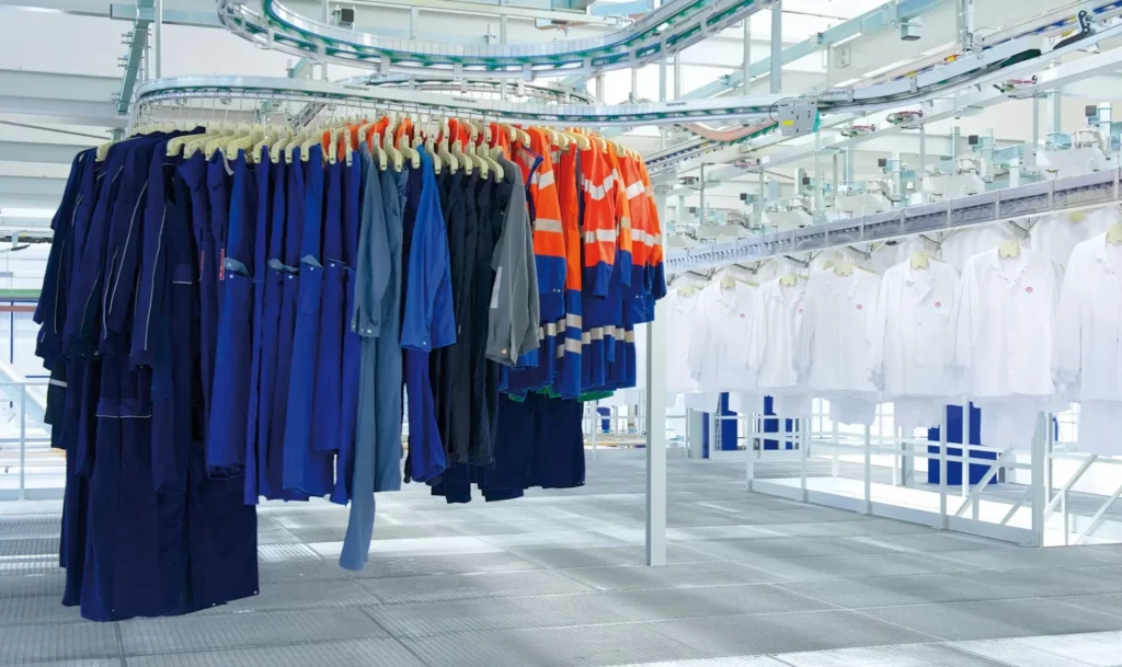 Berufskleidung verschiedener Branchen auf einer automatisierten Förderanlage im Bardusch Textilservice, sortiert und mit RFID-Chips ausgestattet.