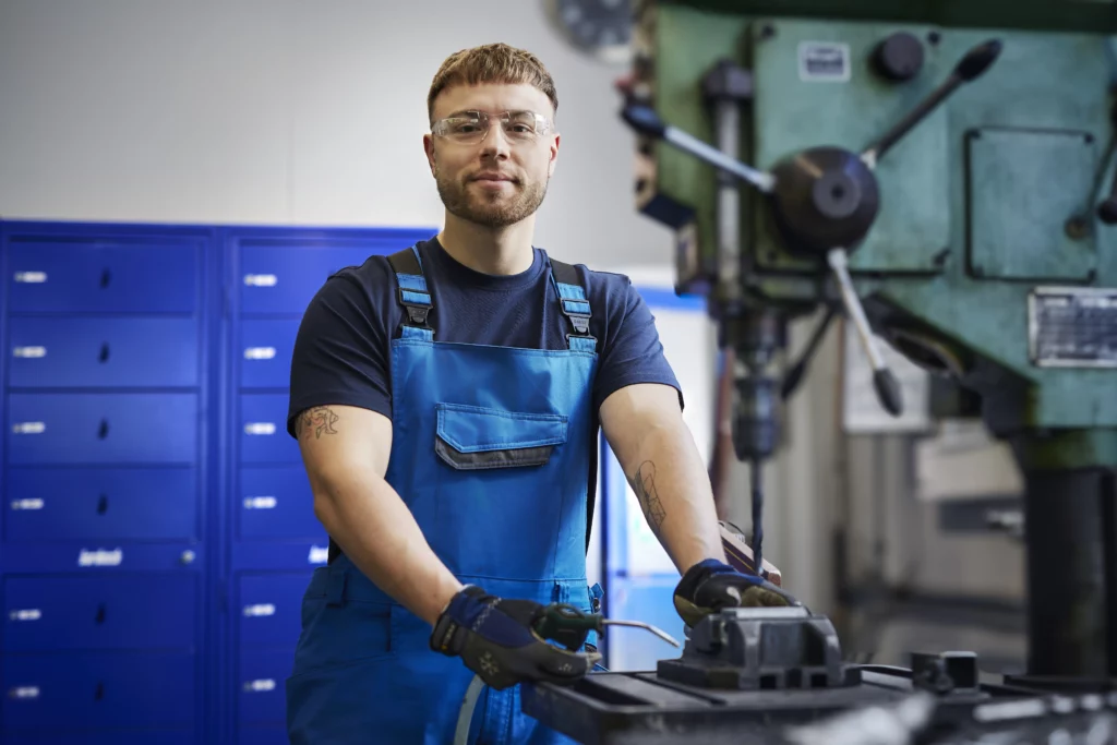Mitarbeiter in blauer Arbeitskleidung steht an einer Maschine – persönliche Schutzausrüstung und Sicherheitsregeln in der Industrie.
