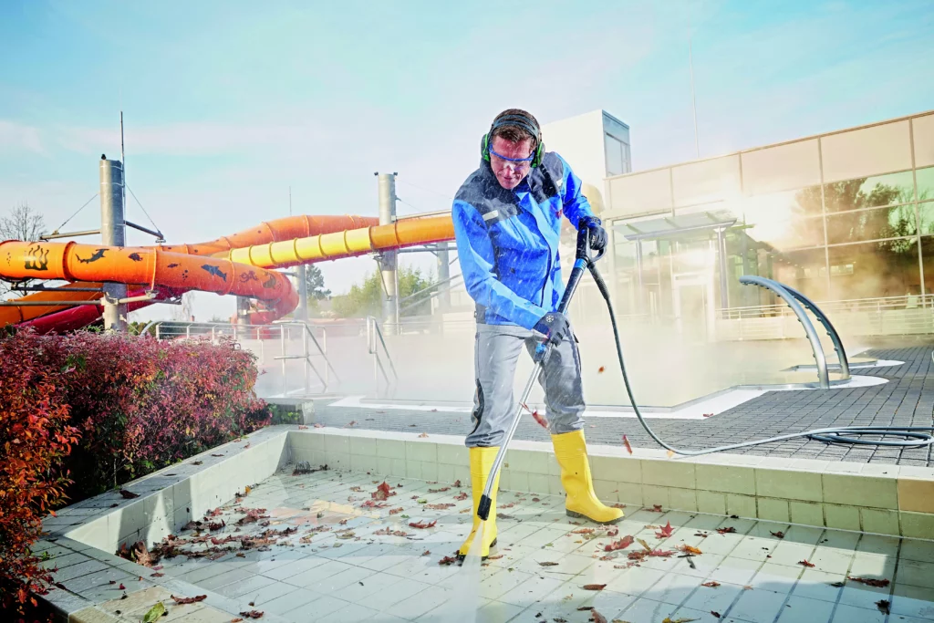 Mitarbeiter reinigt Außenbereich mit Hochdruckreiniger – Schutzkleidung und Arbeitssicherheit nach ISO 45001.