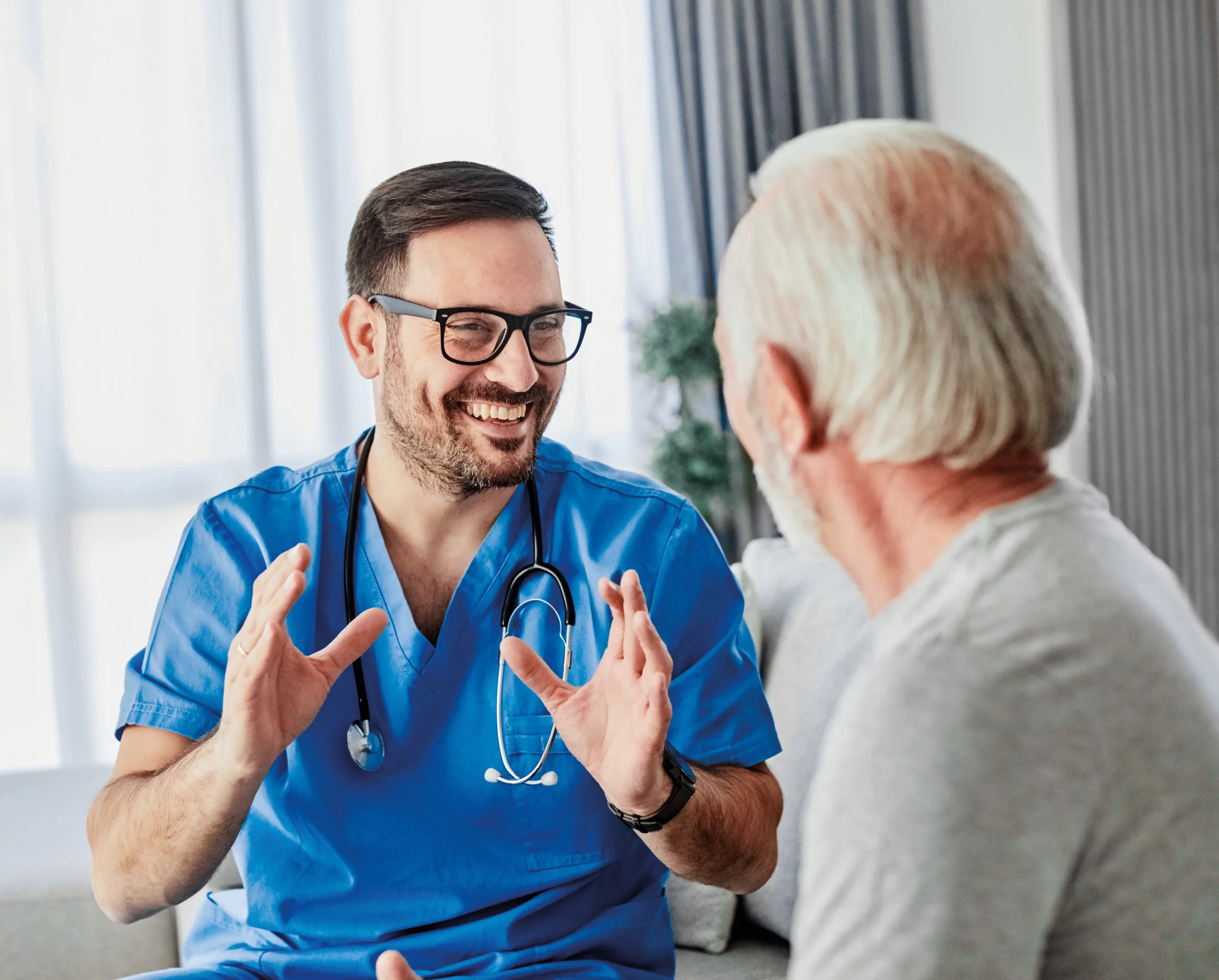 Pflegekraft im Kasack im Gespräch mit einem Bewohner