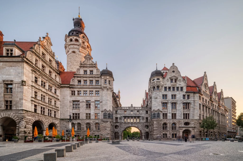 Stadtansicht des Neuen Rathauses in Leipzig mit historischer Fassade, Türmen und dem Platz davor in der Abenddämmerung.
