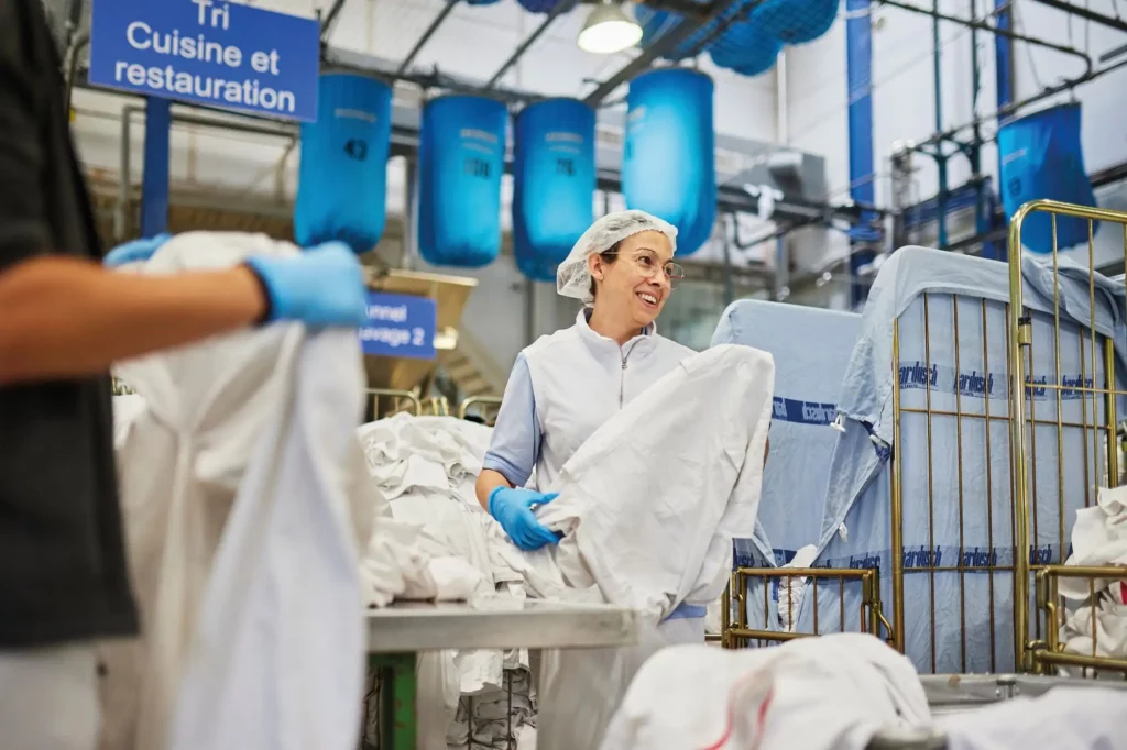 Bardusch Mitarbeiterin in hygienischer Arbeitskleidung bei der professionellen Textilpflege und Wäschelogistik in der Industriewäscherei.