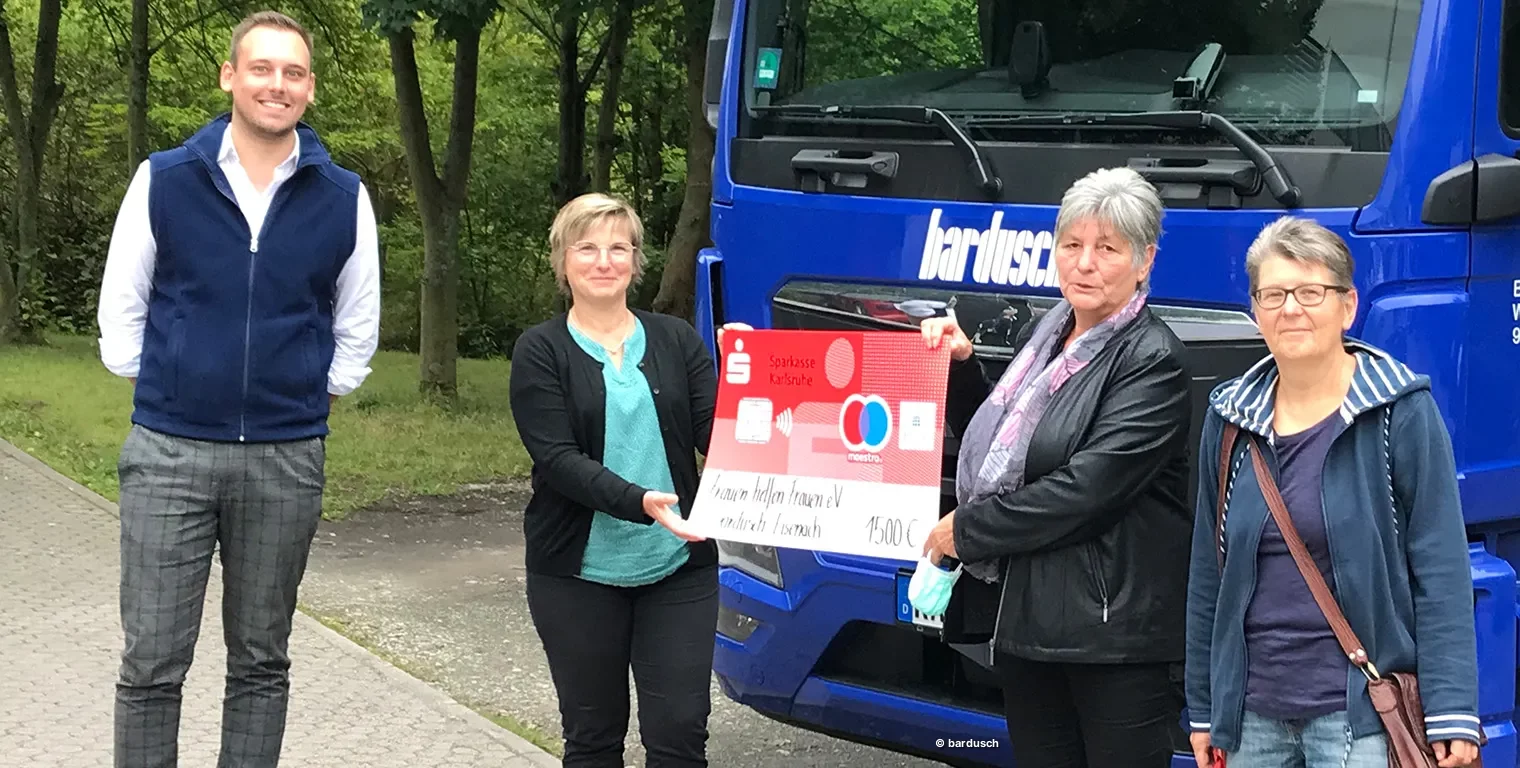 Vier Personen (ein Mann und drei Frauen) stehen vor einem blauen Bardusch-Lkw. Eine der Frauen hält einen großen symbolischen Scheck über 1.500 Euro für das Frauenhaus in Eisenach.