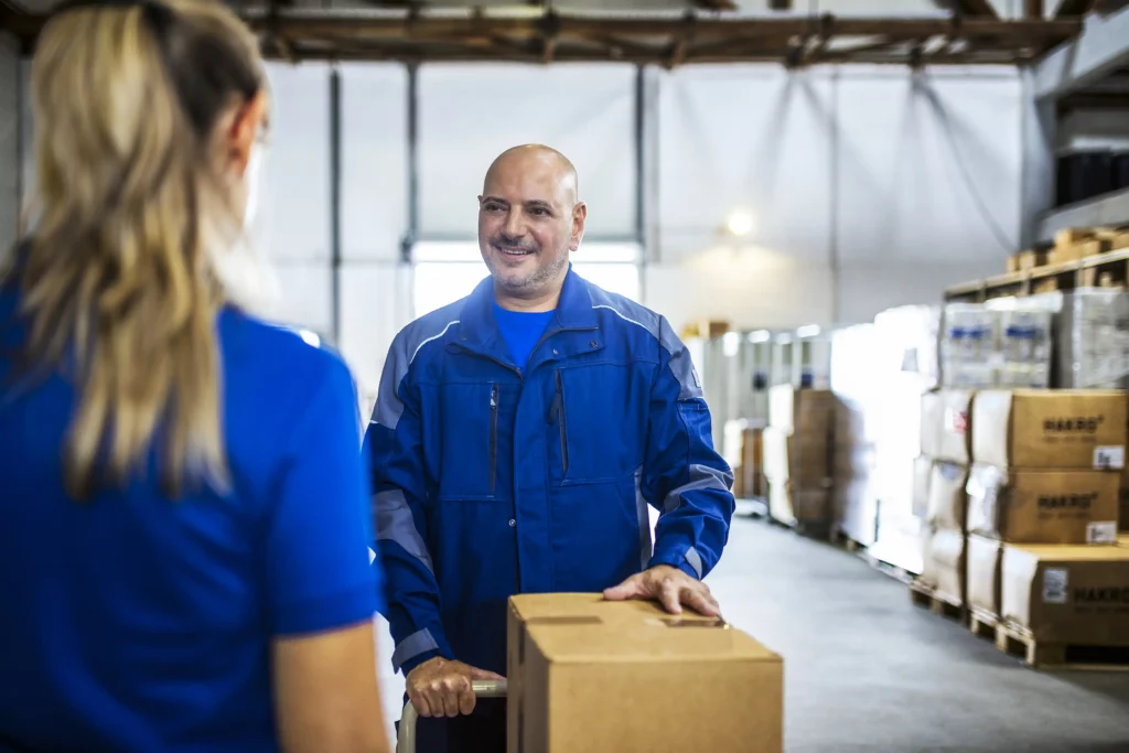 Arbeitskleidung im betrieblichen Alltag Zwei Mitarbeiter sprechen im Lager über Arbeitskleidung