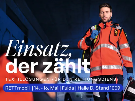 Rettungssanitäter in orangefarbener Einsatzkleidung steht unter einer Unterführung; Werbebanner mit Infos zur RETTmobil-Messe und Textillösungen für den Rettungsdienst.