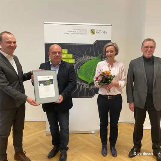 Auszeichnung: EMAS-Zertifizierung der Bardusch Niederlassung in Dresden Vier Personen (Wolfram Günther, Karsten Riep, Janette Trautmann und Dr. Andreas Sperl) stehen in einem Innenraum beisammen. Wolfram Günther überreicht eine Urkunde für die erfolgreiche EMAS-Zertifizierung an Karsten Riep und Janette Trautmann.