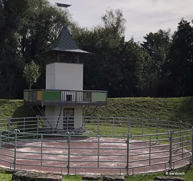 Eine runde Aussichtsplattform oder ein Turm mit einem umzäunten Gelände in einem parkähnlichen Gelände.