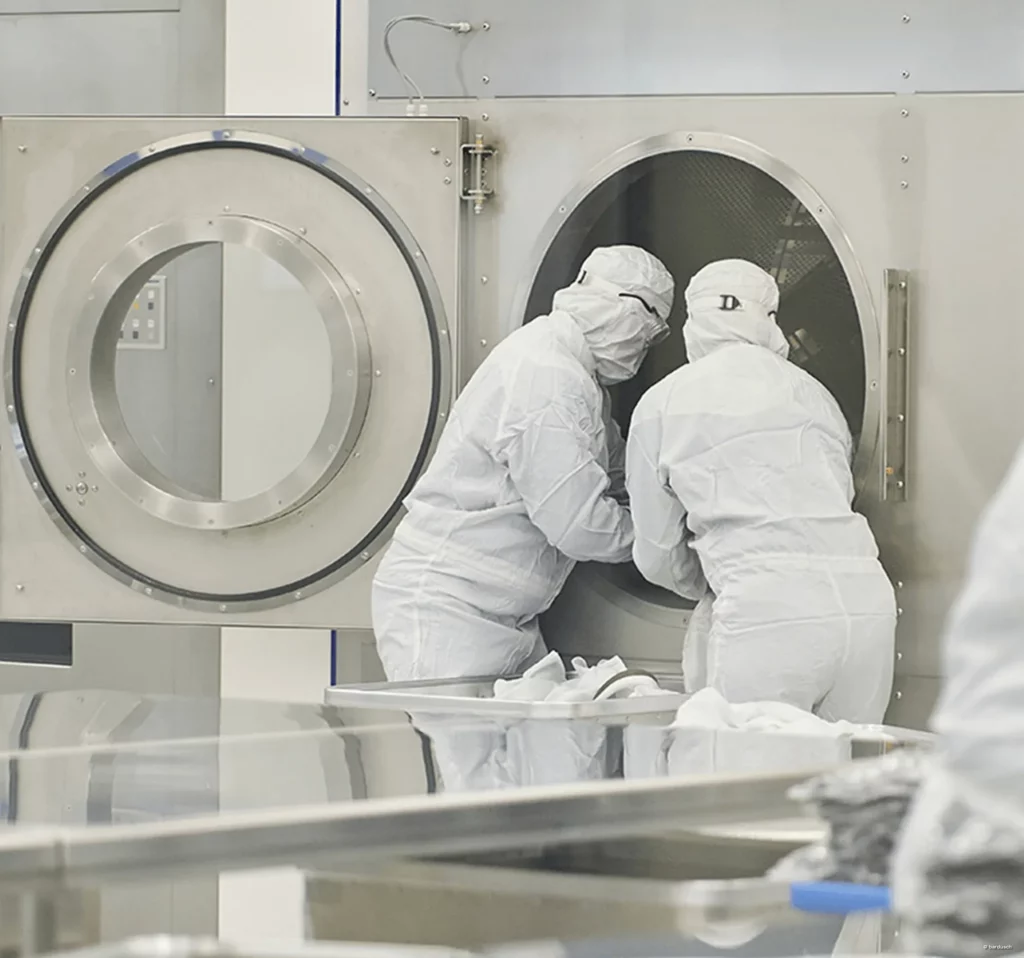 Zwei Mitarbeiter in Reinraumanzügen beim Aufbereiten an einer Industriewaschmaschine