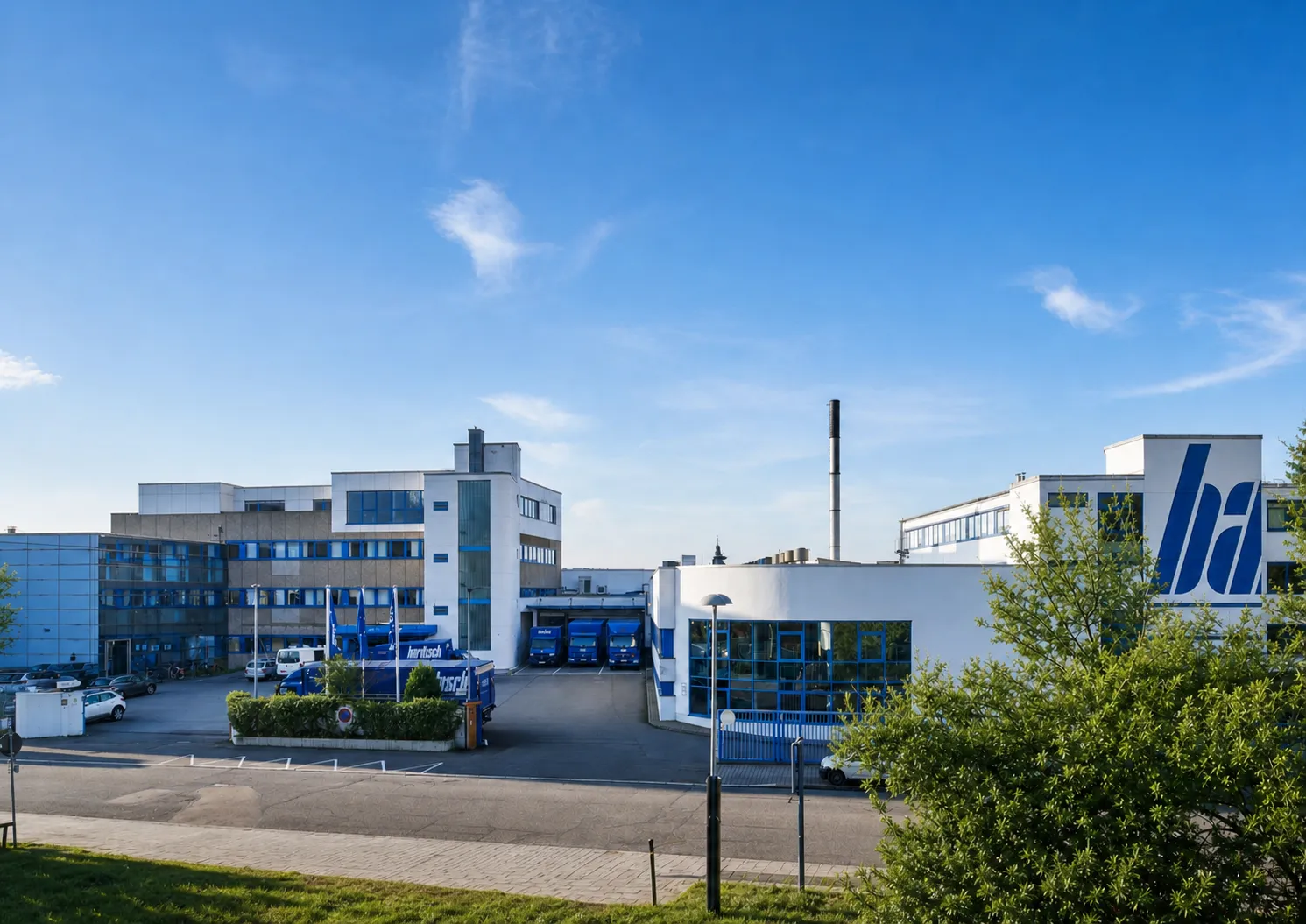 Außenansicht des Bardusch-Standorts Ettlingen: modernes Unternehmensgebäude in Weiß und Blau mit Firmenfahrzeugen auf dem Betriebsgelände und dem Bardusch-Logo an der Fassade